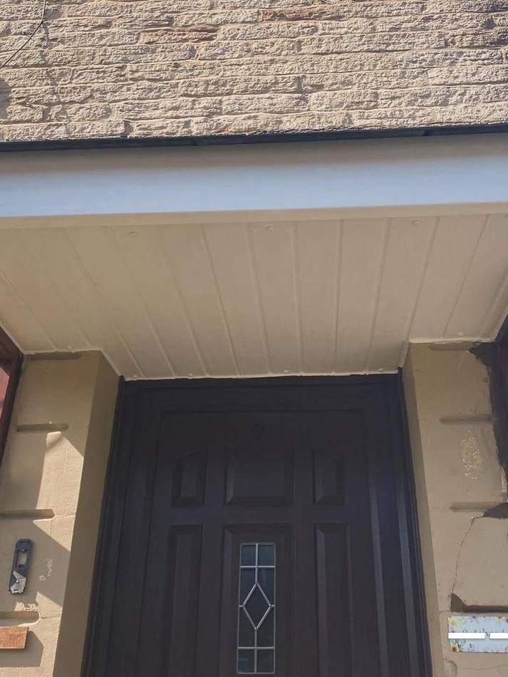 Entrance canopy on a stone house with decayed timber brackets and cracked render around the doorway