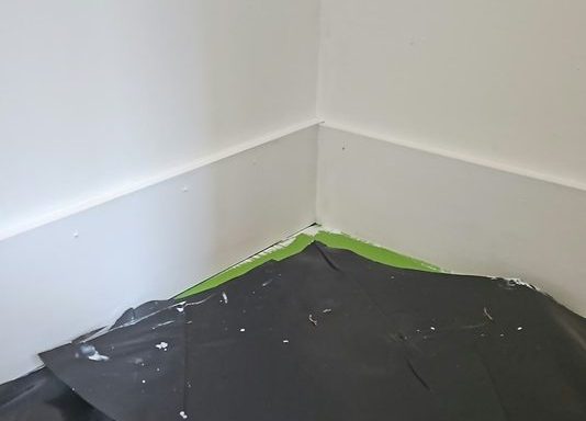 Room with the floor fully sheeted and the wall newly finished, protection laid before work begins