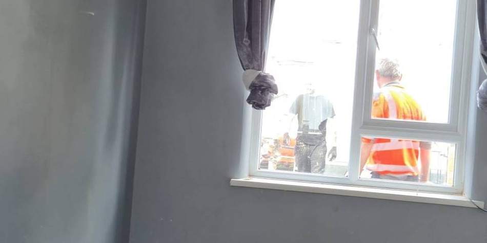 Bedroom in an occupied home with plaster hacked back to brick at low level, ready for the underlying cause to be treated and the wall replastered