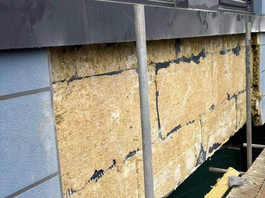 Rainscreen panels removed from a high-rise elevation exposing mineral wool insulation and perished membrane behind