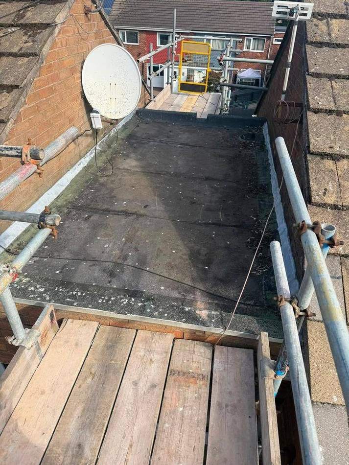 Flat roof between two pitched roofs with old felt patched, blistered and holding water