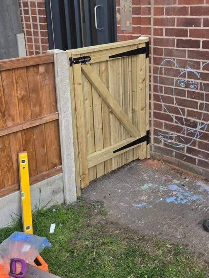 New timber gate hung on black strap hinges between a fence and a brick wall