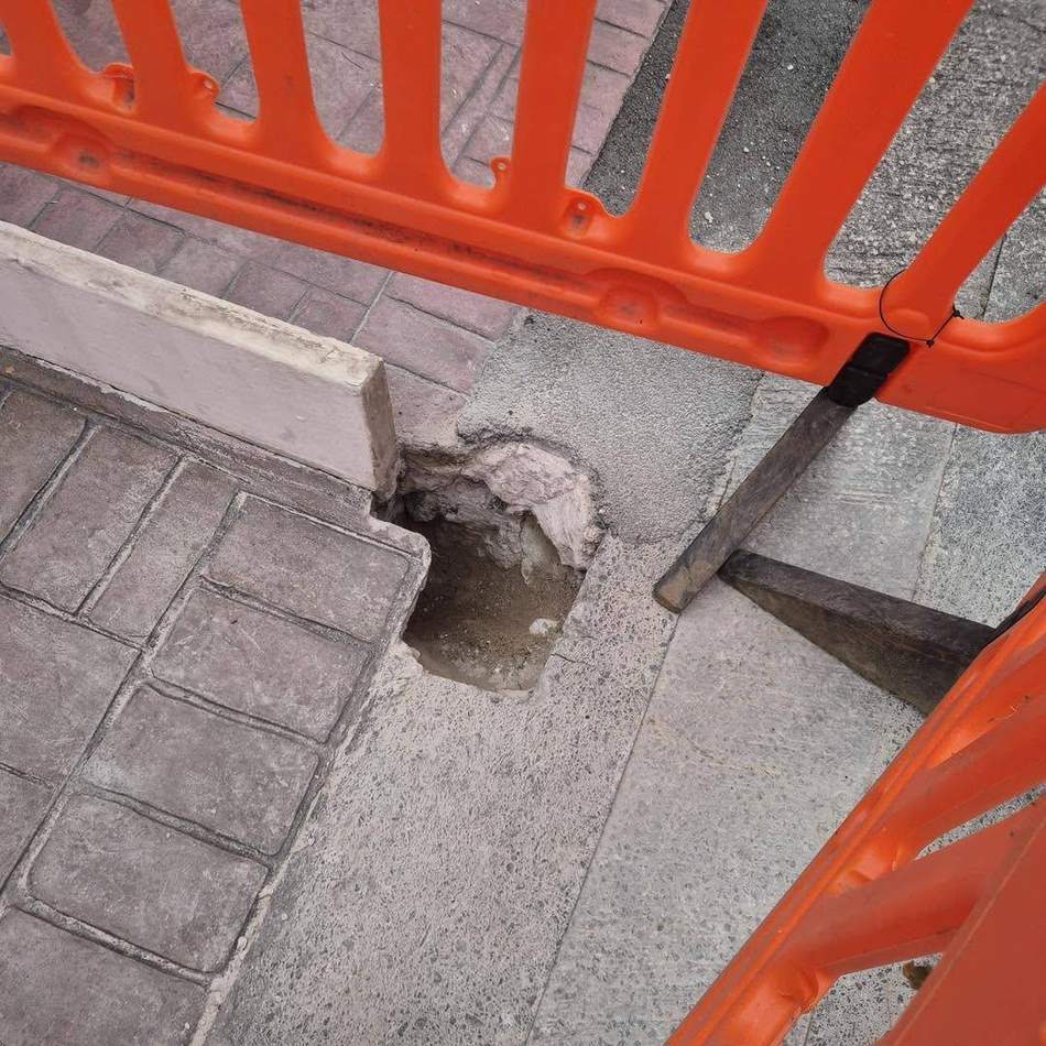 Footway paving lifted at the kerb line to reach the drainage beneath