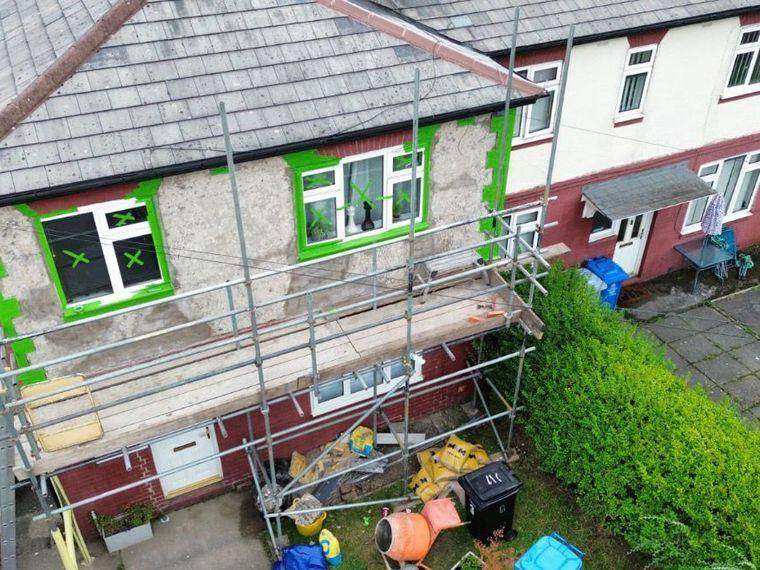 Scaffolded semi-detached house with render stripped back and windows masked ready for re-rendering