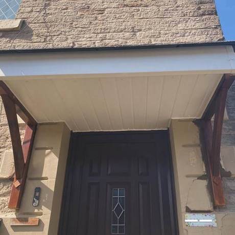 Entrance canopy on a stone house with decayed timber brackets and cracked render around the doorway