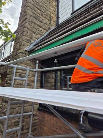 Operative working on the fascia above a commercial shopfront from a scaffold