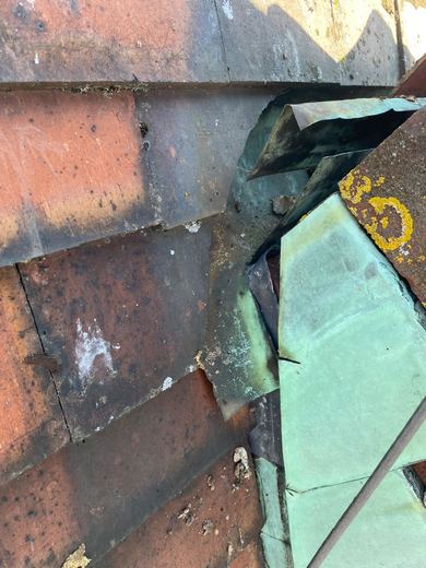 Original copper flashing at an abutment, oxidised and torn, lifted clear of the tiles it should be dressed over