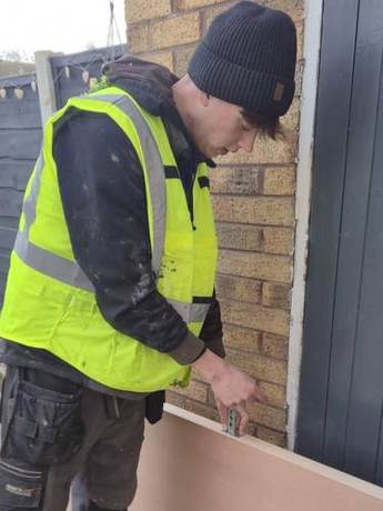 Joiner fitting ironmongery to a new internal door leaf resting against a brick wall