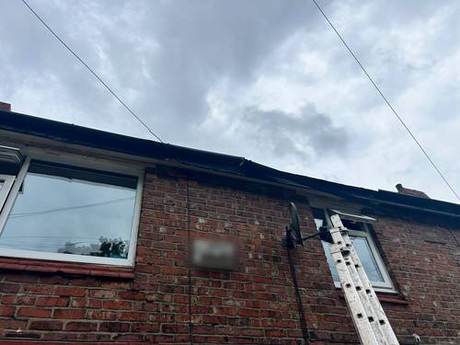 Ladder set against the rear elevation of a brick house at eaves level
