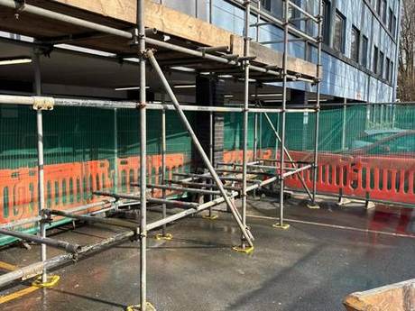 Scaffold erected against a multi-storey block behind hoarding and pedestrian barriers