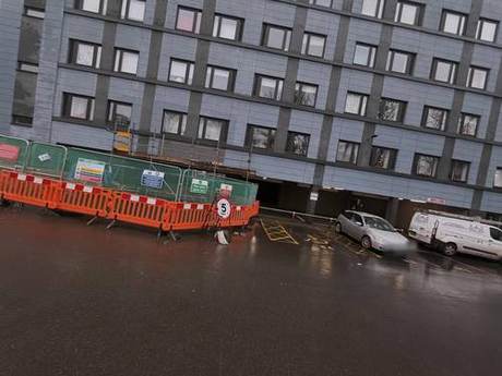Multi-storey residential block with pedestrian barriers and site hoarding set up at ground level