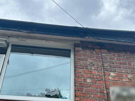 Original dark fascia and soffit above a window, weathered and split, before replacement