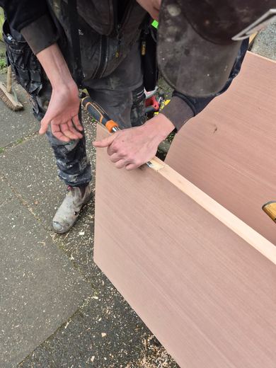 Two operatives cutting a fire door leaf to the opening on a bench outside