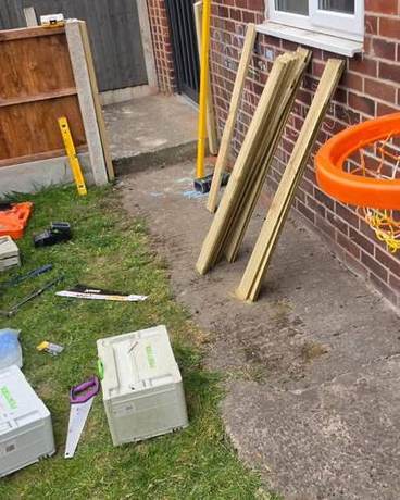 Fence rails and tools set out on the grass beside a house before the fence is built