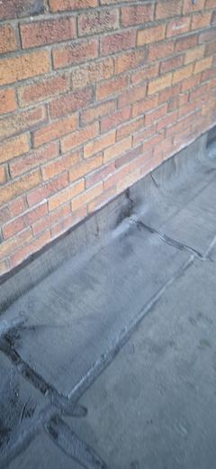 New timber firrings laid across a flat roof deck to create the fall, with the covering dressed up to the brick wall behind