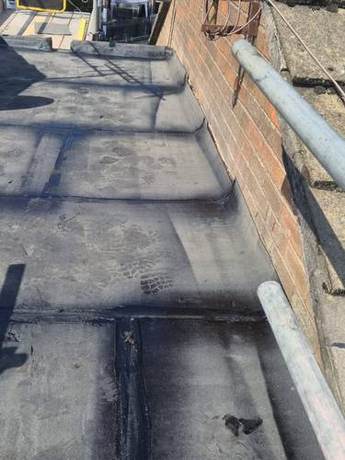 First layer of torch-on felt laid across a flat roof and dressed up the parapet upstand, with bitumen bled out along every lap to prove the seams are sealed