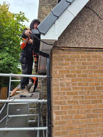 Operative fixing a new black gutter to a newly capped fascia from a mobile tower
