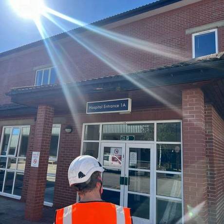 Operative in hi-vis and helmet outside a hospital entrance before starting work
