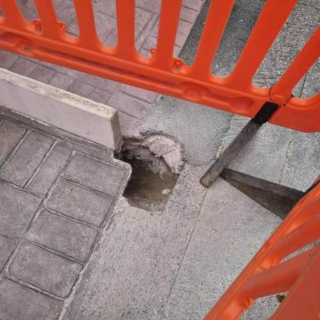 Paving opened up at the kerb line beside a pedestrian barrier to expose the void beneath