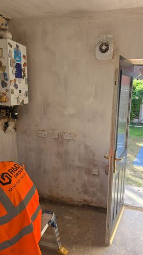 Operative in hi-vis plastering a hallway wall beside an open back door