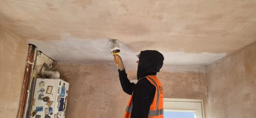 Operative working overhead with a trowel, skimming a ceiling