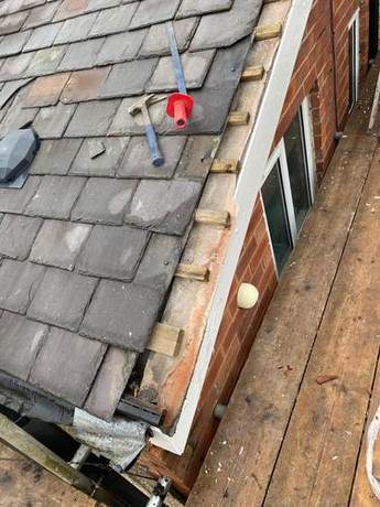 Slate roof slope with tools laid out and slates being spliced in across the pitch