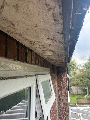 Painted timber soffit and fascia blackened and breaking up along the eaves of a brick house before renewal