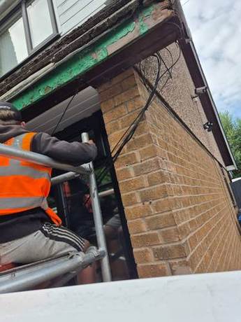 Operative on a mobile tower stripping decayed painted timber from the eaves of a brick house