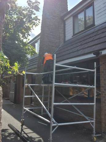 Mobile tower set up in a rear yard with an operative working at roof level above