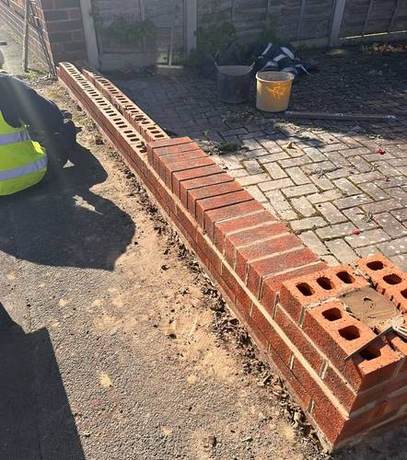 New brickwork being built off the footing along a boundary line with bricks stacked ready alongside