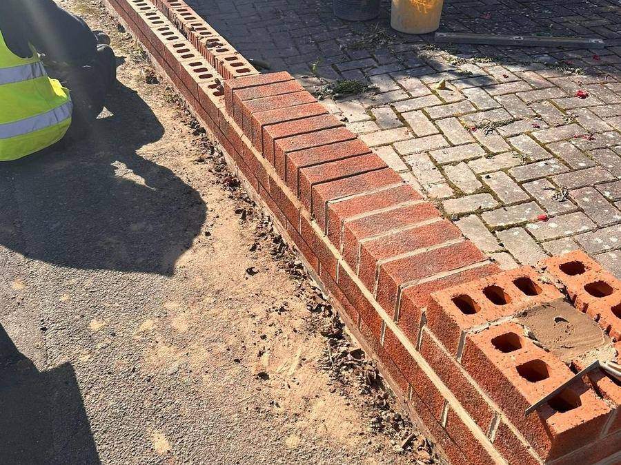 New brickwork being built off the footing along the boundary line with bricks stacked ready alongside